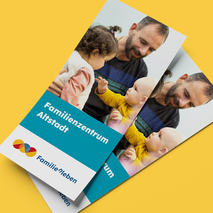 familienleben-print Zwei freigestellte Flyer des Familienzentrum Altstadt auf gelbem Hintergrund. Die schlichten Flyer zeigen ein Foto eines dunkelhaarigen Vaters mit einem Kleinkind und einem Baby.