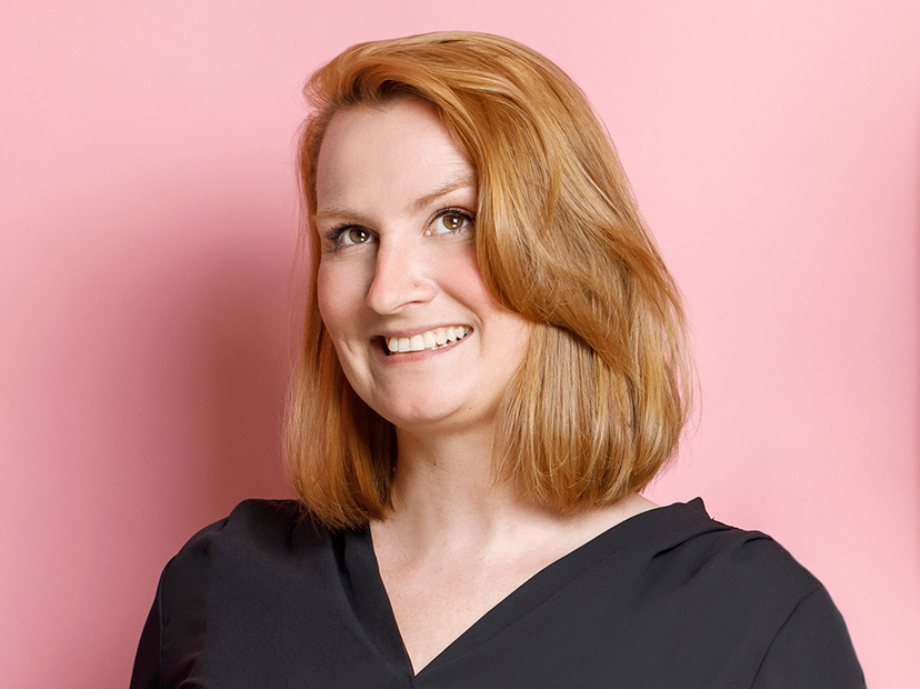 katy-schmitt Ein Portraitfoto von Katy Schmitt vor pinkfarbenem Hintergrund. Katy hat rötliche, halblange Haare, lächelt und guckt schräg nach rechts oben.
