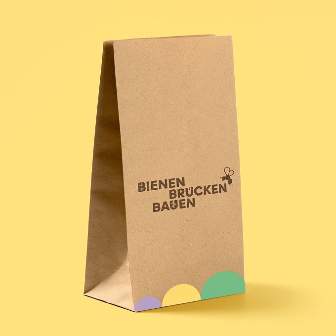 web_BBB_2 Freigestelltes Bild einer braunen Papiertüte aus Kraftpapier auf gelbem Hintergrund. Auf der Tüte ist das Logo des Projektes