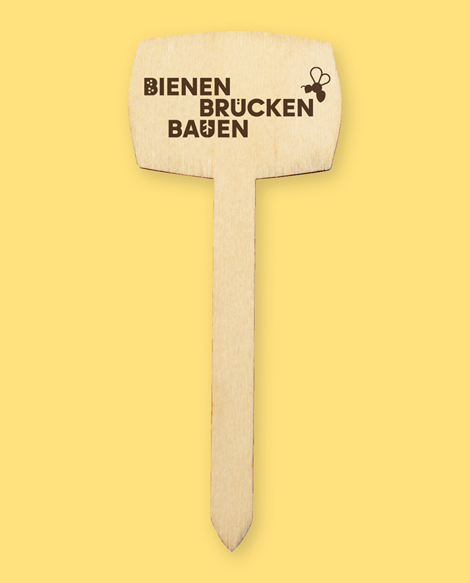 web_BBB_3 Ein freigestelltes Bild eines Pflanzsteckers aus Holz auf gelbem Hintergrund. Auf dem Pflanzstecker ist das Logo des Projektes
